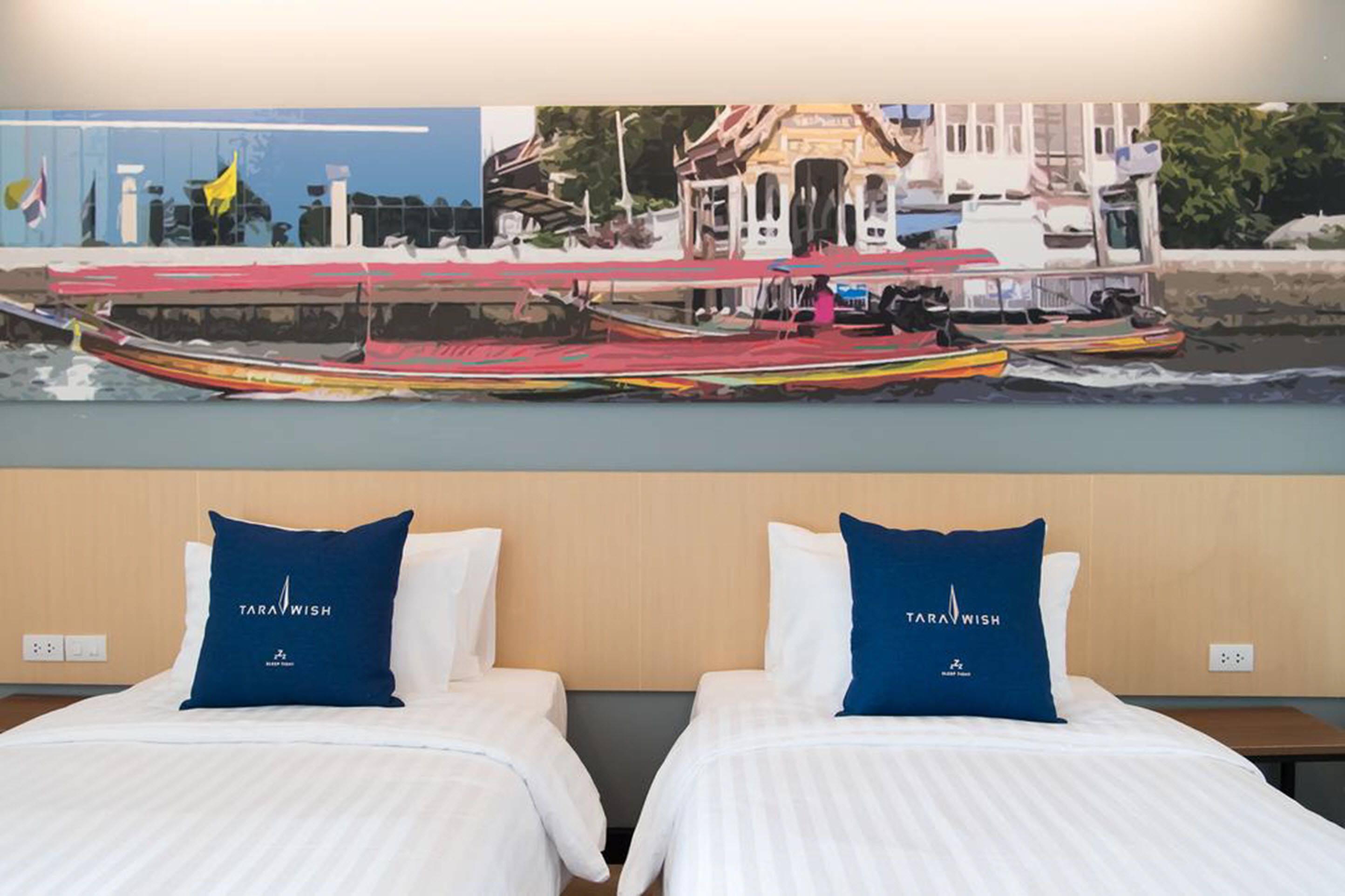 A hotel room with two beds, each with a pillow labeled "TARAWISH."