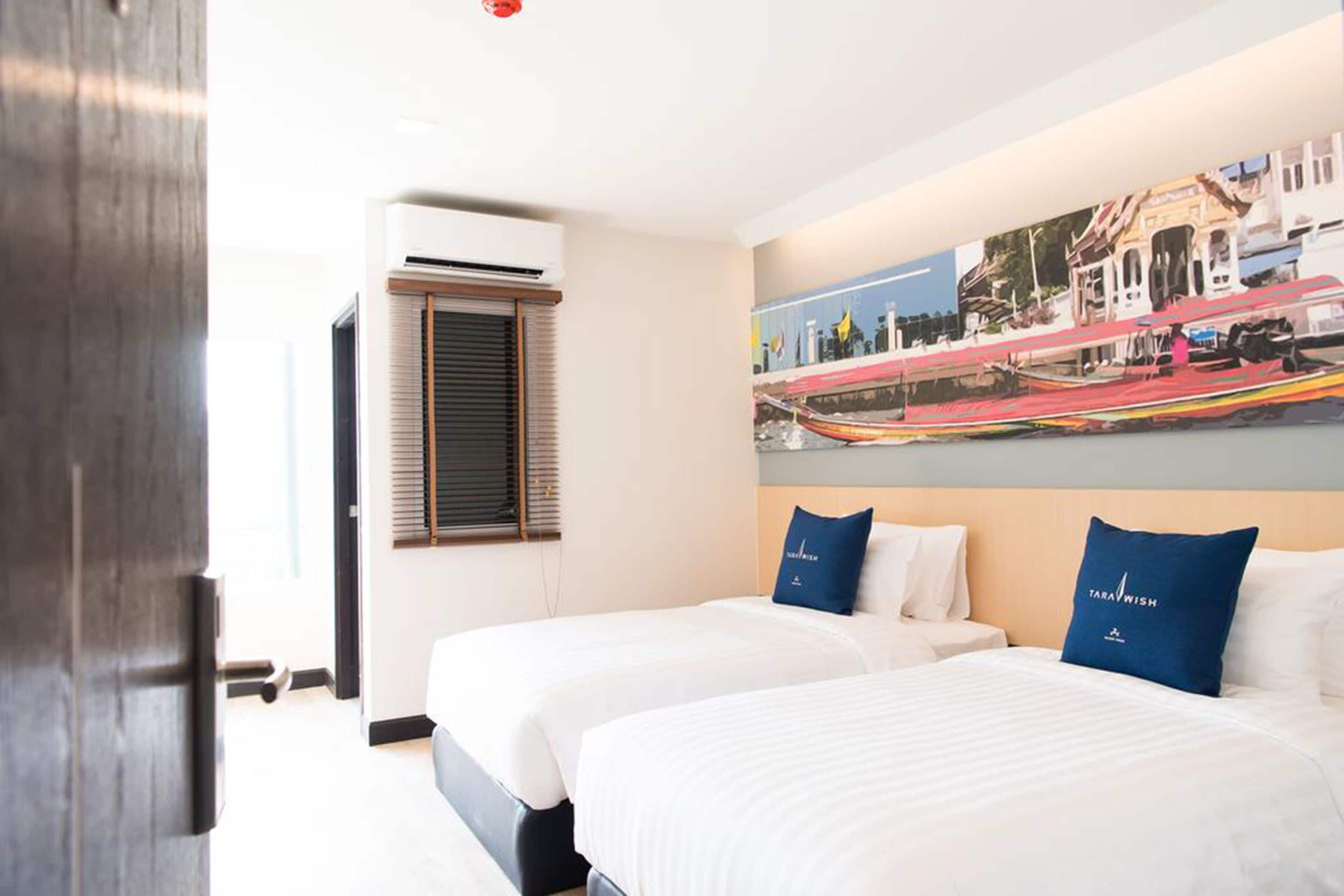 A hotel room with two beds, a large window with blinds, an air conditioning unit, and a wall mural.
