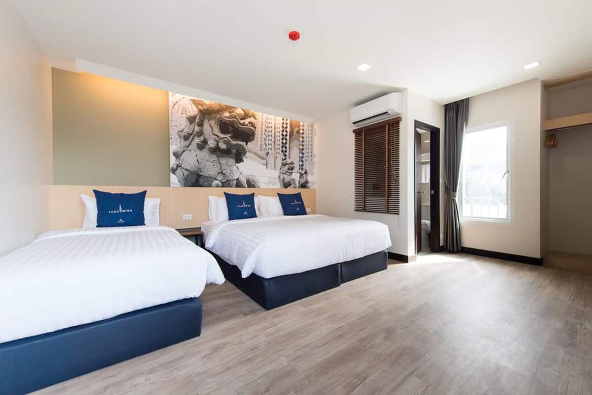 A hotel room with two beds, a large wall mural, an air conditioning unit, a window with curtains, and a wardrobe.