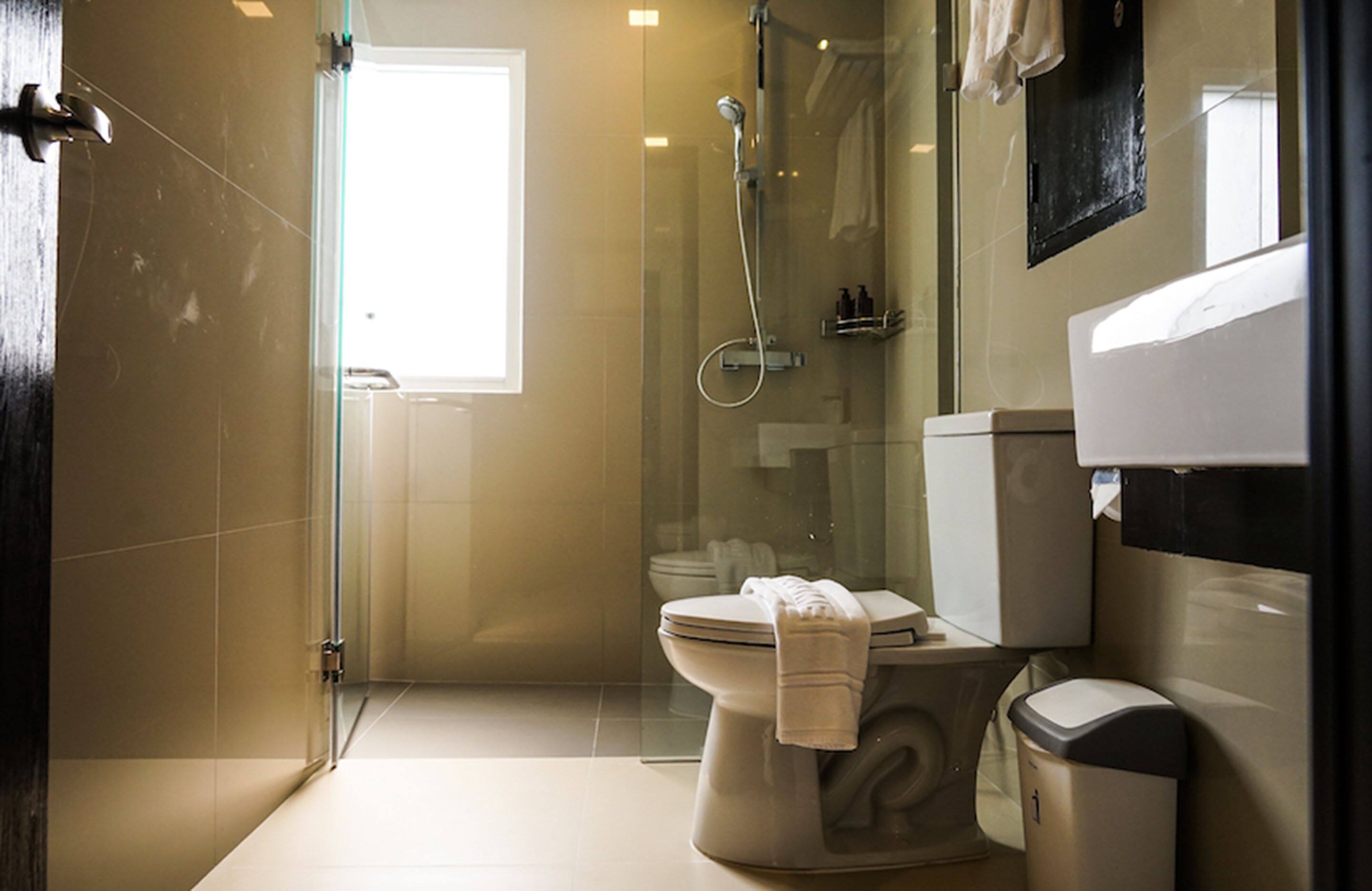 A modern bathroom with a glass-enclosed shower, a toilet, and a trash bin.