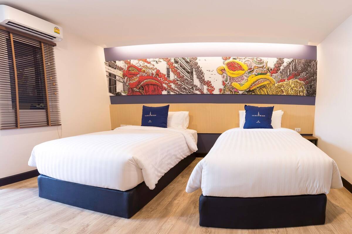 A hotel room with two beds, a large wall mural, and a window with blinds.
