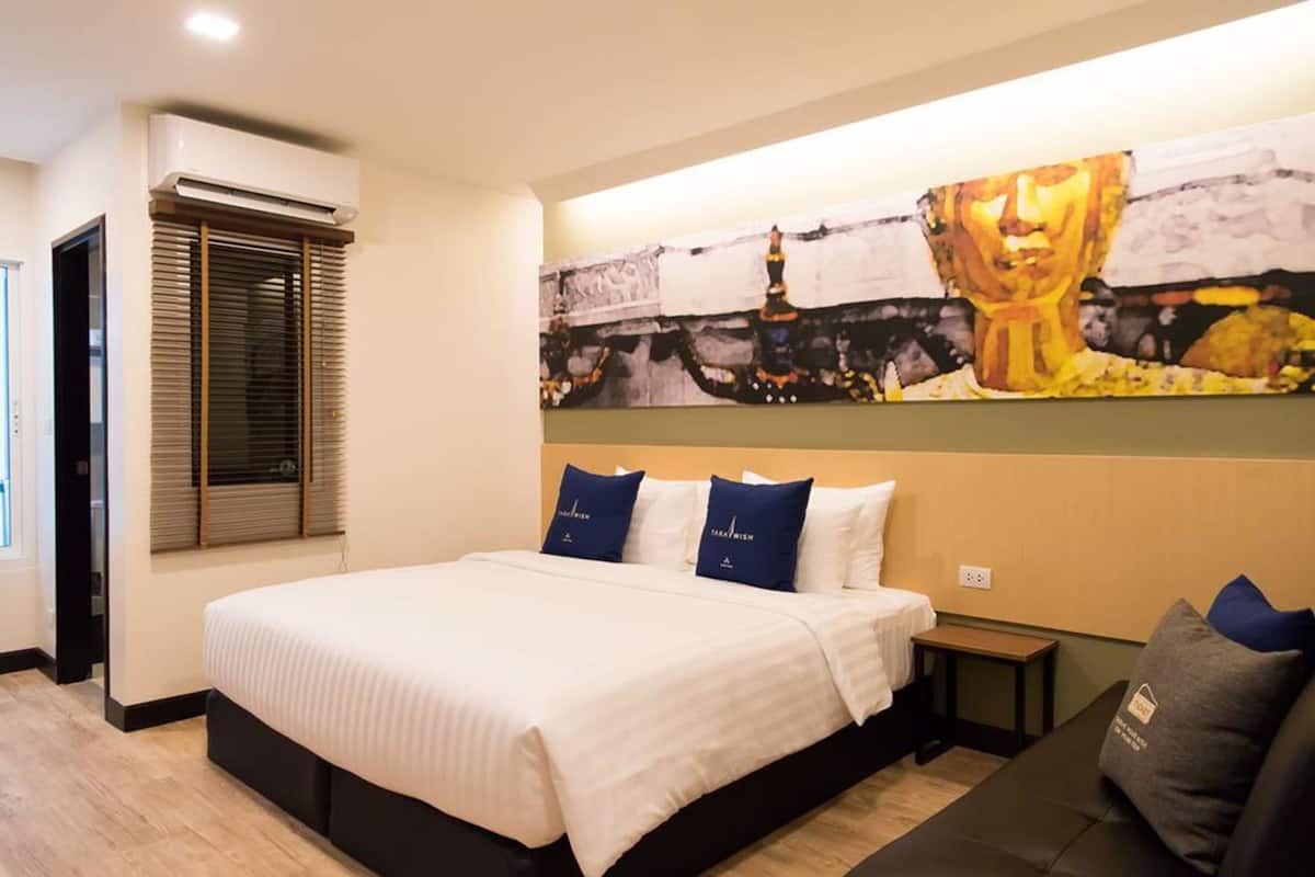 A hotel room with a large bed, a nightstand, a wall-mounted air conditioner, and a large painting above the bed.