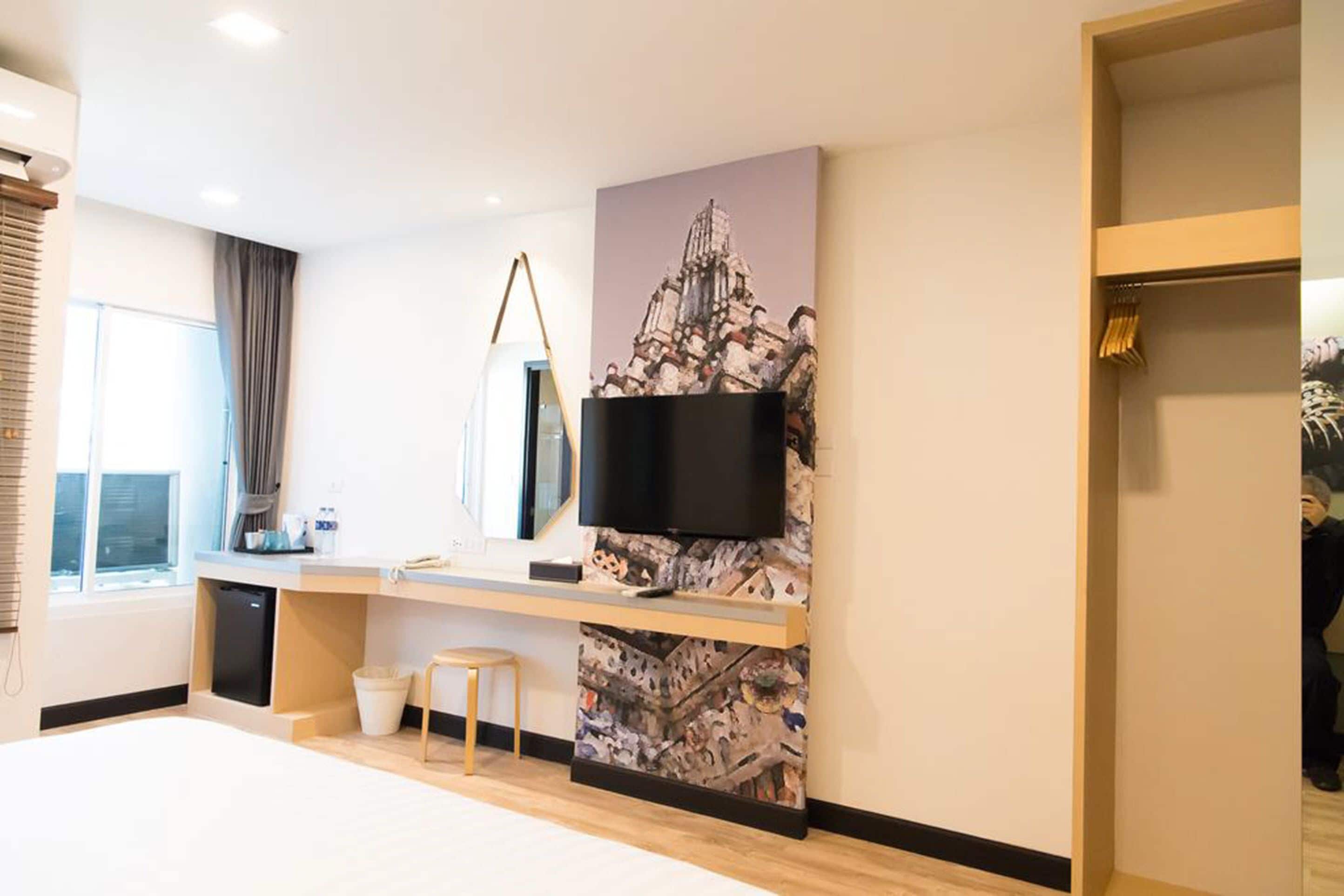 Une chambre d’hôtel moderne dotée d’un grand lit, d’un téléviseur à écran plat fixé à un mur texturé, d’un petit bureau avec une chaise et d’une fenêtre avec des rideaux.