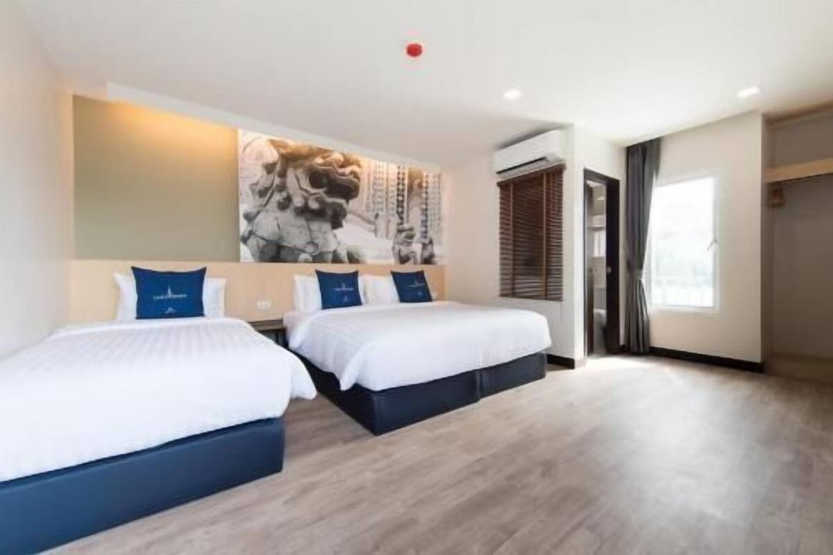 A hotel room with two beds, a large abstract painting on the wall, and a window with curtains.