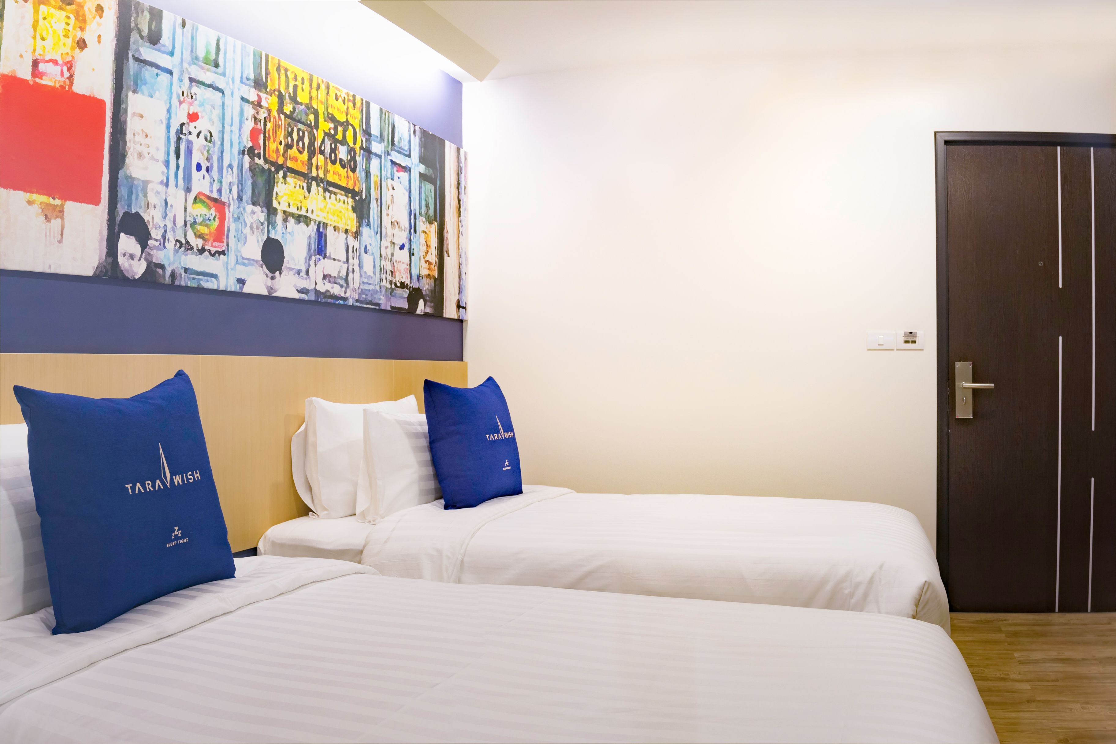 Ein Hotelzimmer mit zwei Betten, einem großen abstrakten Gemälde an der Wand und einer dunklen Holztür.