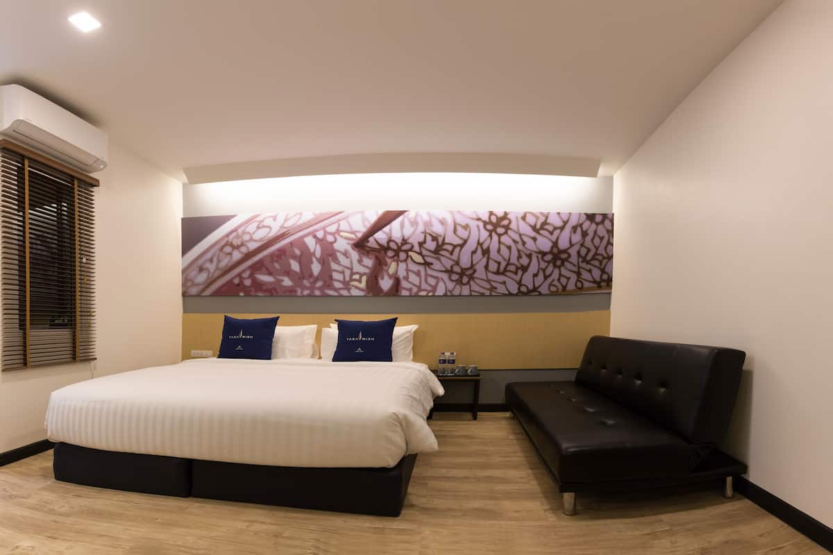 A modern hotel room with a large bed, a sofa, and a wall-mounted artwork.