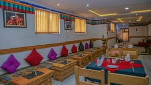 A restaurant with wooden tables and benches, colorful cushions, and framed pictures on the walls. - Himalayan Retreat Karzoo (Leh)
