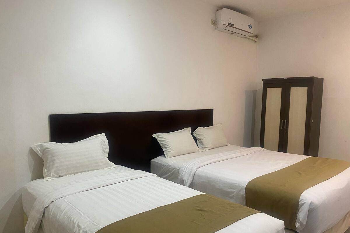 Quarto de hotel com duas camas, um guarda-roupa e um aparelho de ar condicionado.