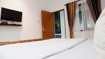Un dormitorio con cama, televisor montado en la pared, puerta de madera y ventana con cortinas.