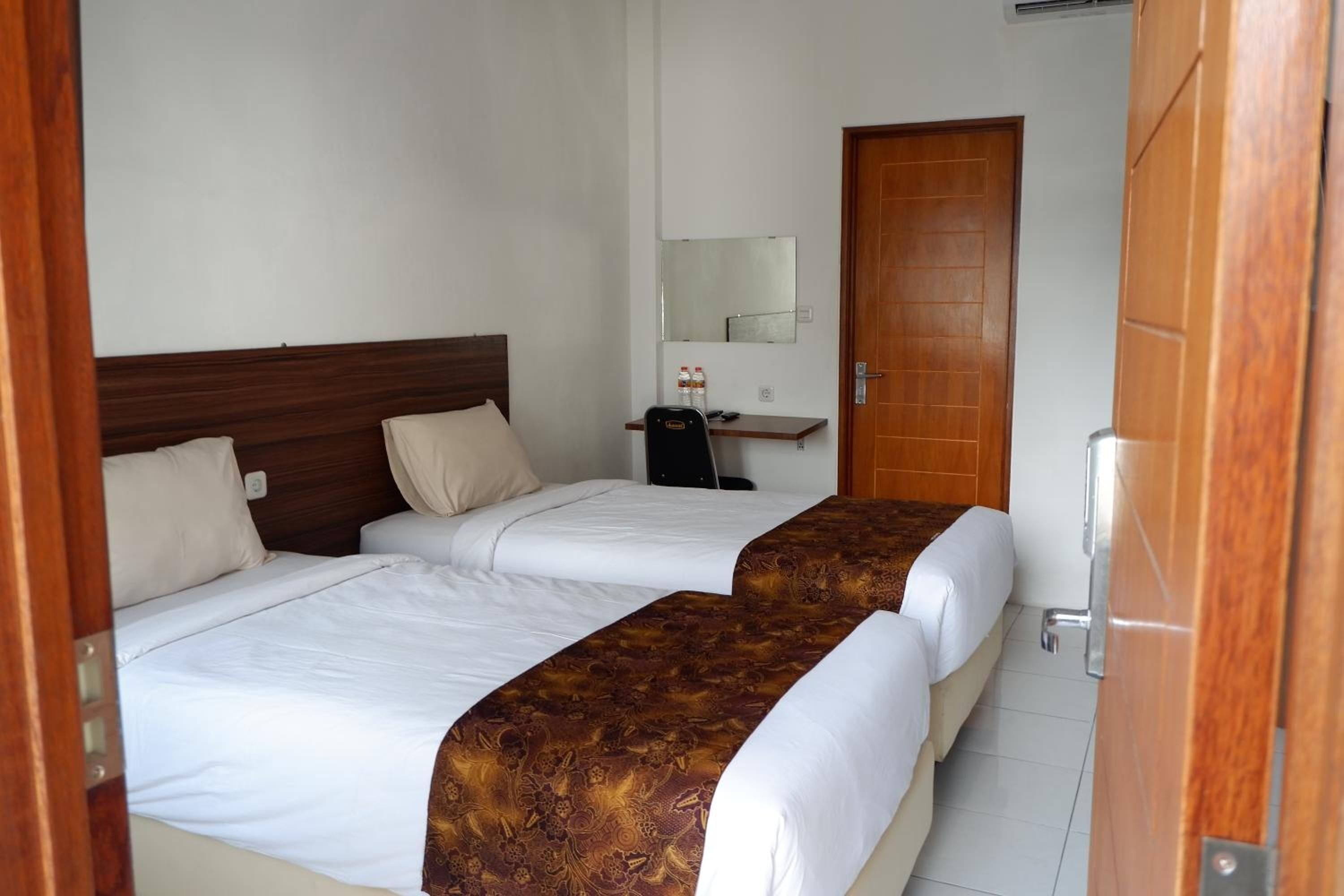A hotel room with two beds, a wooden headboard, a desk with a chair, a mirror, and a door.