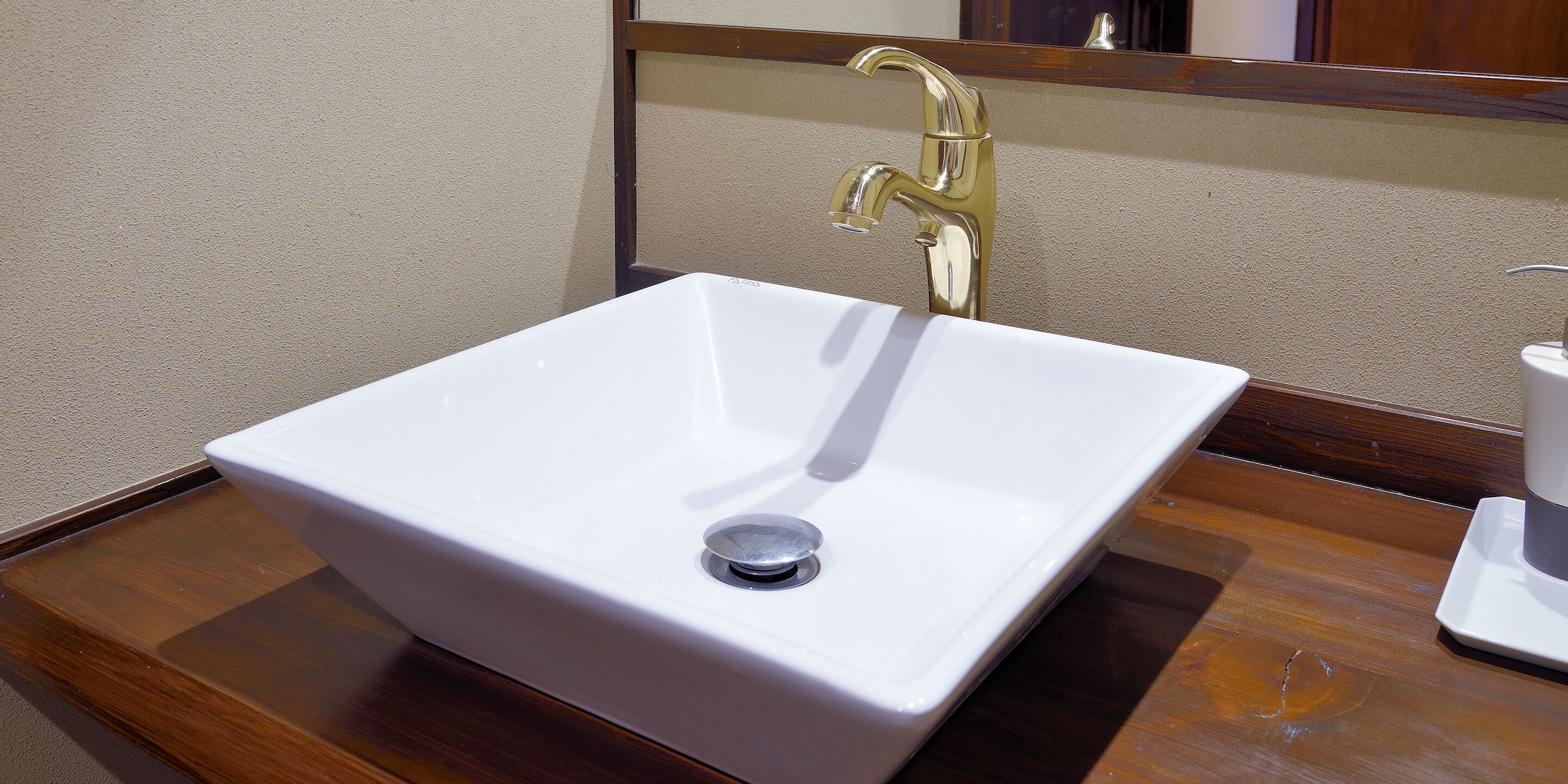 A white rectangular sink with a single faucet, a mirror above it, and a wooden countertop.
