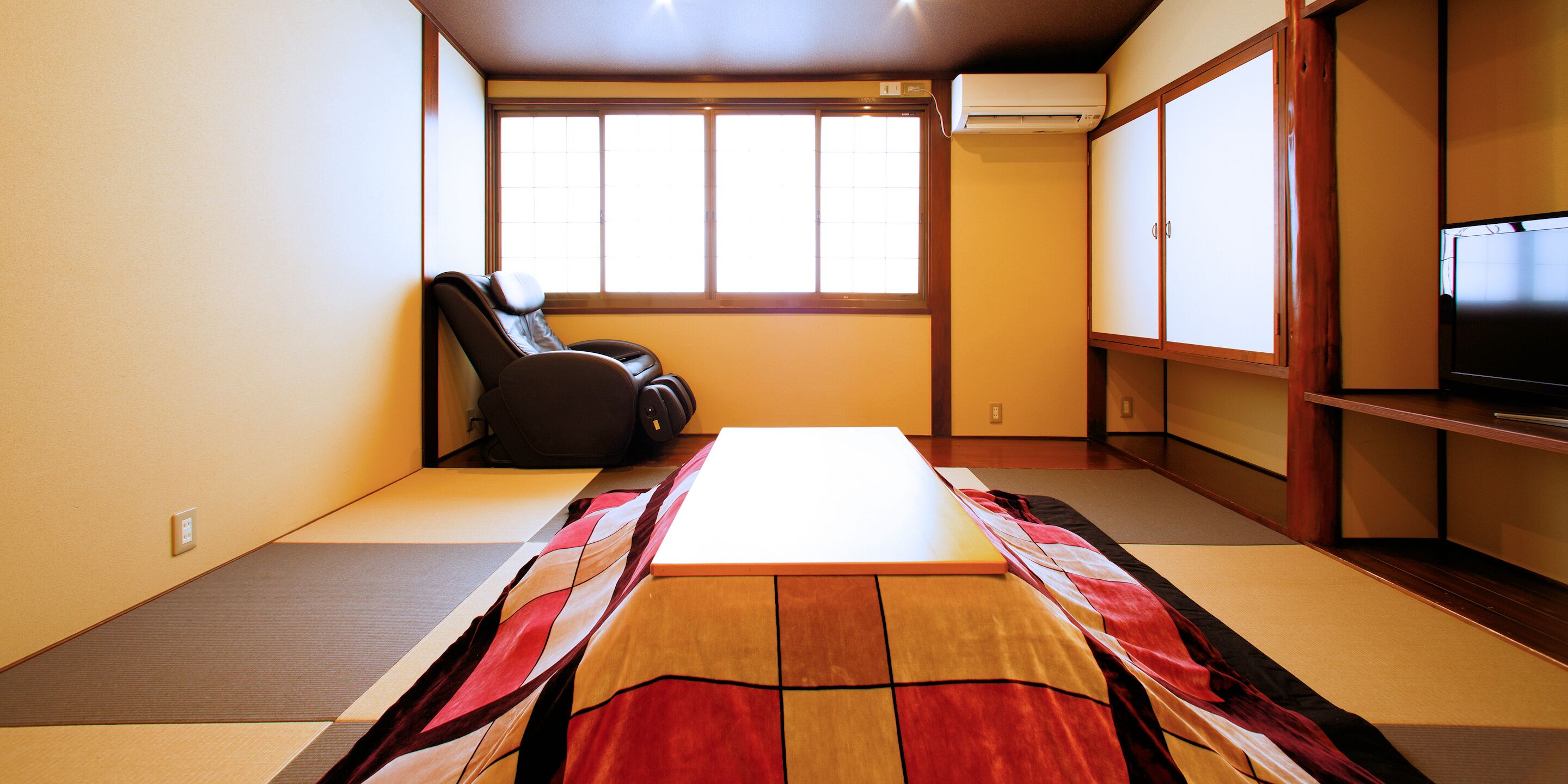 A room with tatami flooring, a futon bed, a massage chair, a television, and sliding doors.