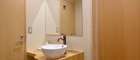 Un baño con tocador de madera, un lavamanos blanco y un espejo encima.