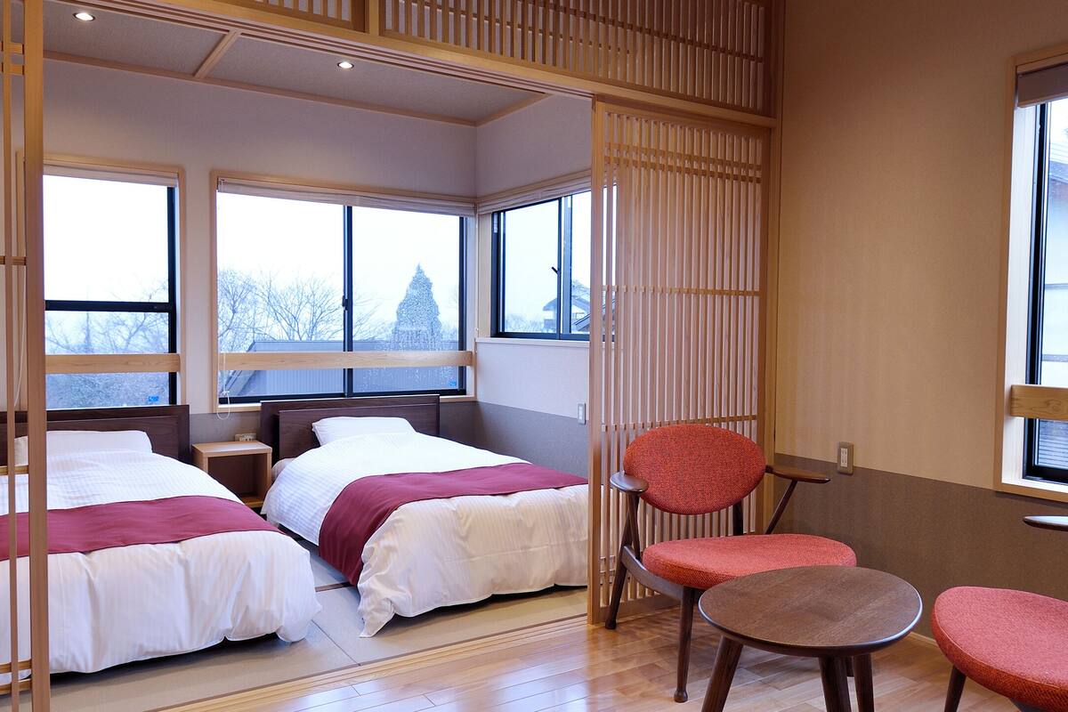 A hotel room with two beds, a seating area with a table and chairs, large windows, and a view of a snowy landscape.