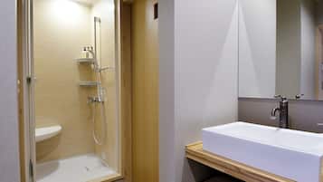 Un baño moderno con ducha a ras de suelo, un lavamanos grande de color blanco y un mueble de tocador de madera.