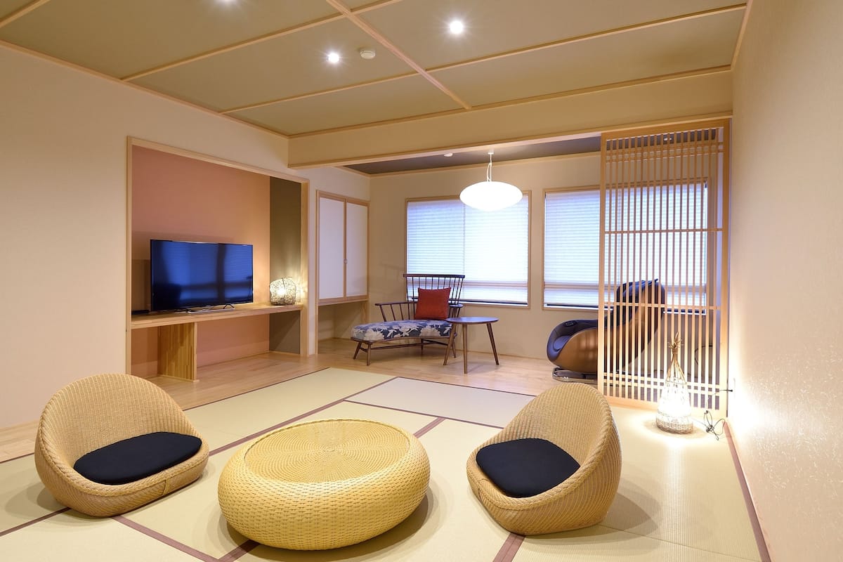 A traditional Japanese-style living room with tatami flooring, a television, a low table, and two tatami chairs.