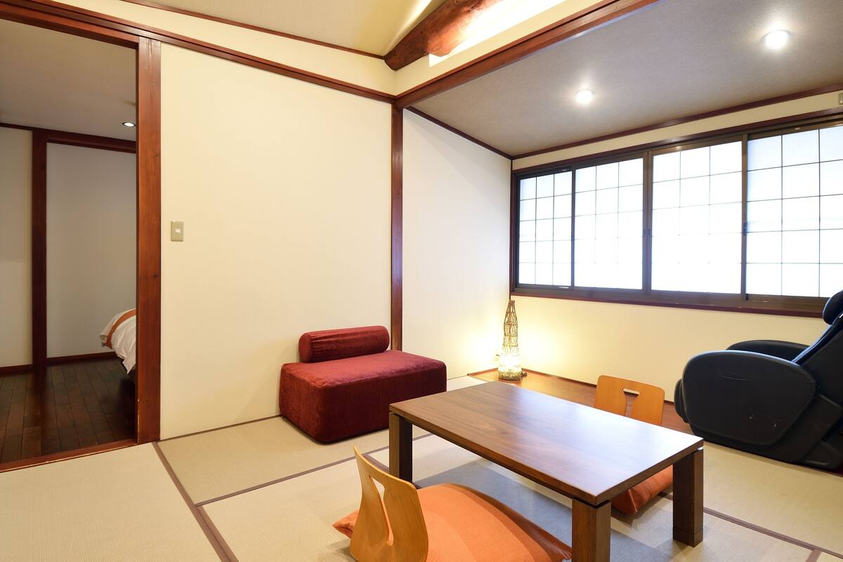 A traditional Japanese room with tatami flooring, a low wooden table, a red sofa, a black chair, and a window with shoji screens.