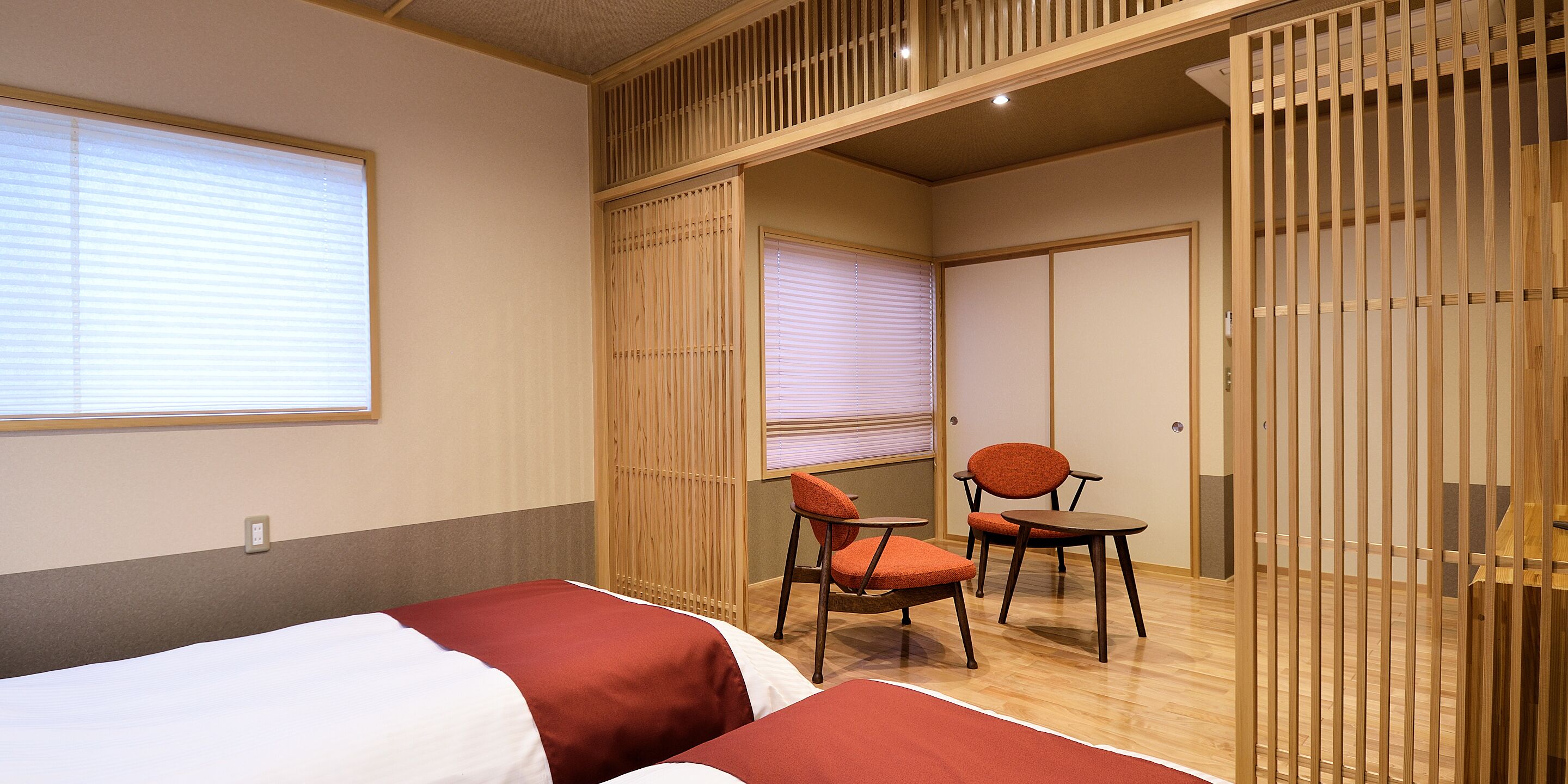 Een hotelkamer met twee bedden, een houten scheidingswand en een kleine tafel met twee stoelen.