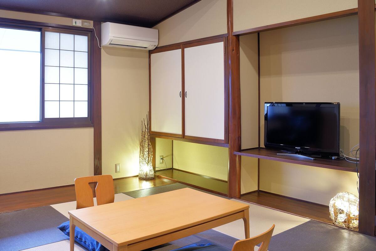 A room with tatami flooring, a massage chair, a television on a wooden stand, and a traditional Japanese-style cabinet.