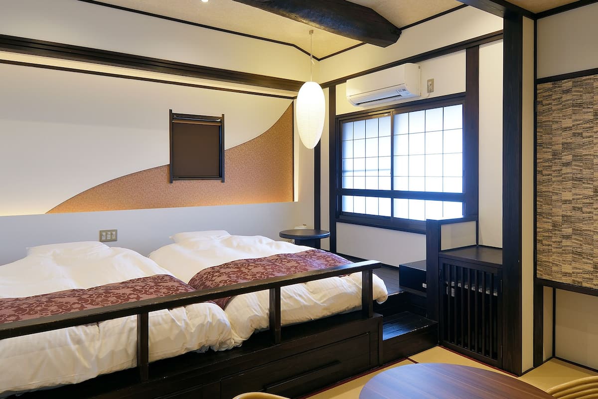 A bedroom with a bunk bed, a small table, a window with a view, and a traditional Japanese-style wardrobe.