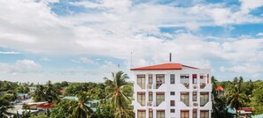 A multi-story building with a red roof, surrounded by palm trees and other greenery.
