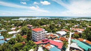 A coastal town with a mix of residential buildings and greenery, a prominent white building with a red roof, and a view of the sea and distant islands. - Rekidhiye Inn (Hithadhoo)
