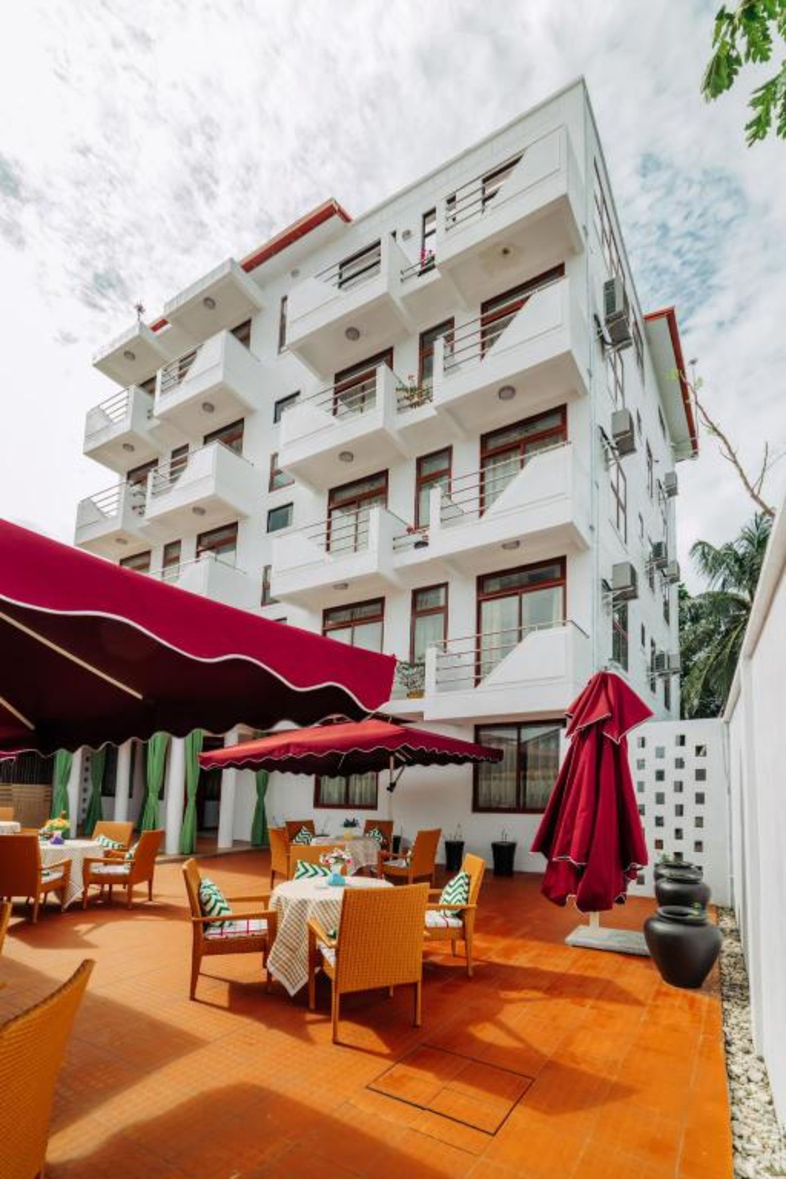Un hotel con mesas al aire libre, varios balcones y un toldo rojo.