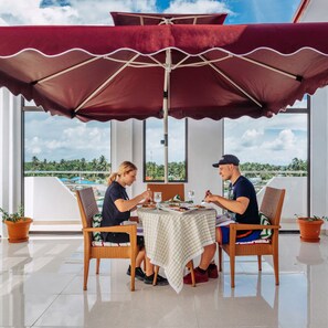 A dining area with a table and chairs under a large umbrella, overlooking a scenic view.
