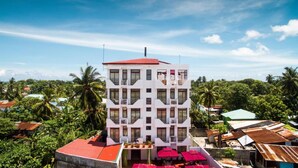 A multi-story hotel with a white facade and red roof, surrounded by lush greenery and palm trees. - Rekidhiye Inn (Hithadhoo)