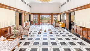 Eine geräumige Lobby mit einem geometrisch gefliesten Boden, einem imposanten Kronleuchter und Blick auf eine gebirgige Landschaft durch große Fenster.