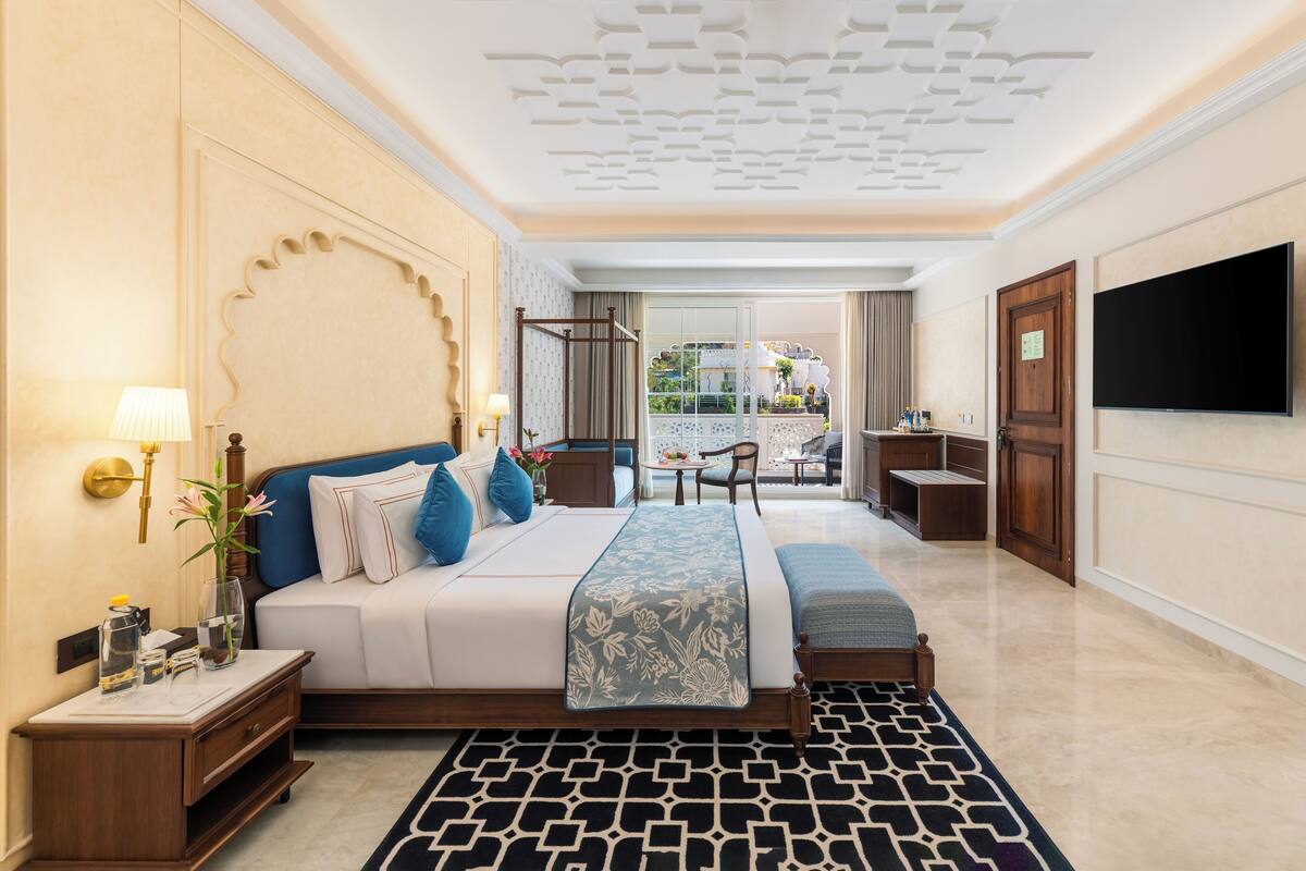 A hotel room with a large bed, a desk, a chair, a TV, and a balcony view.