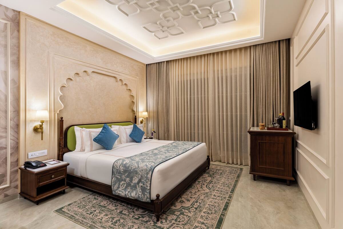A hotel room with a large bed, a nightstand with a telephone, a television on the wall, and a decorative ceiling light fixture.