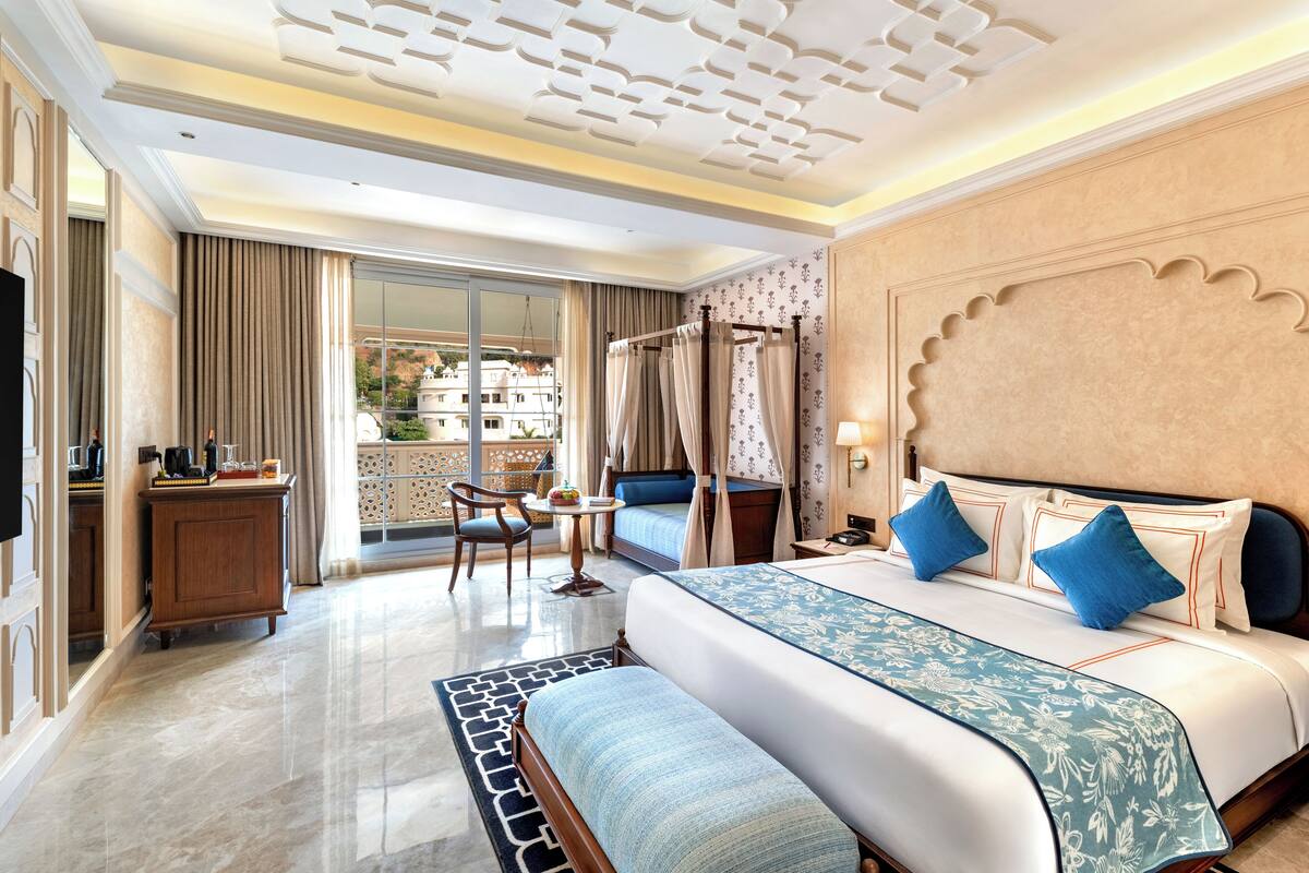 A hotel room with a large bed, a desk, a chair, a small table, and a view of the outside.
