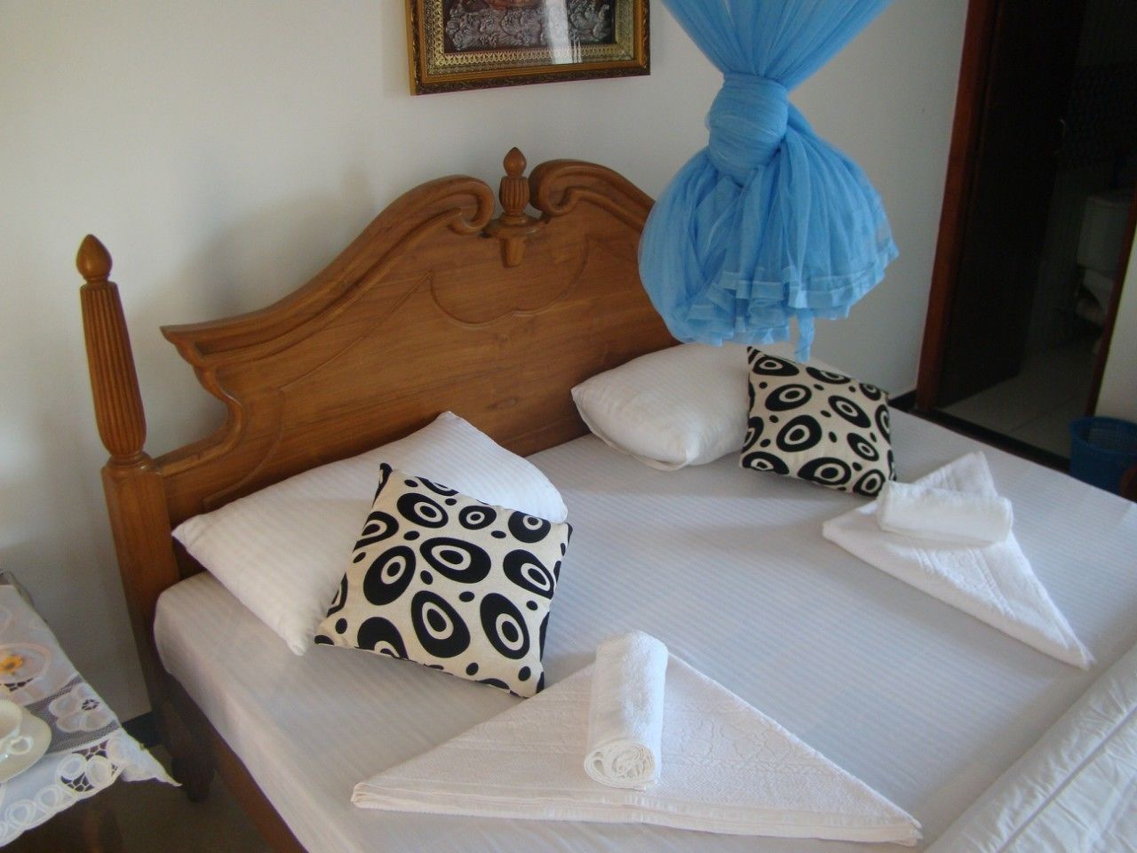 Una cama bien hecha con almohadillas estampadas, cabecera de madera y dosel azul.