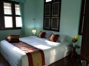 A bedroom with a large bed, a bedside lamp, a window with curtains, and a wall-mounted TV. - Maliwan Holiday Home (Nakhon Si Thammarat)