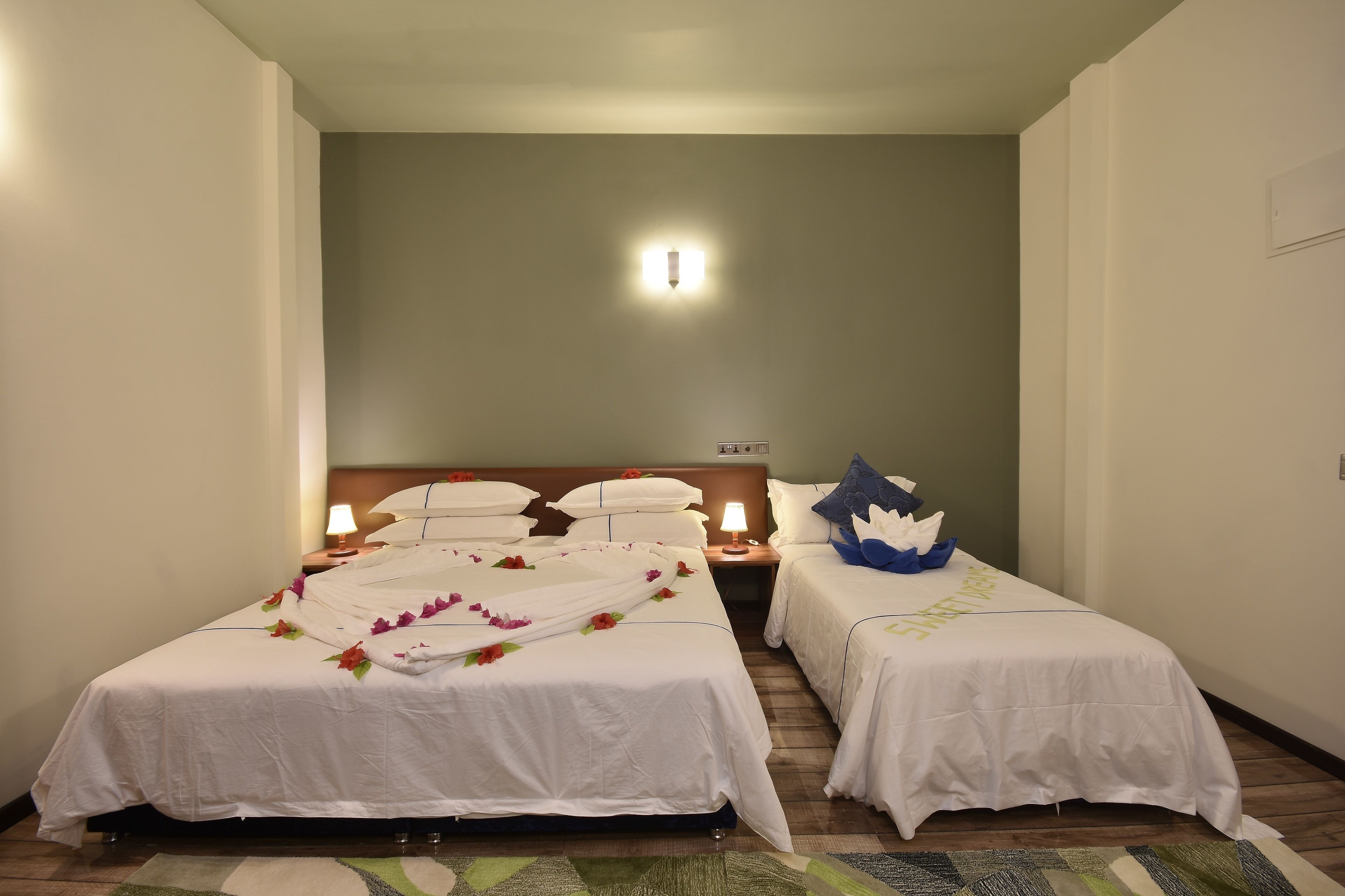 Habitación de hotel con dos camas individuales, una mesita de noche con lámpara y una lámpara de pared.