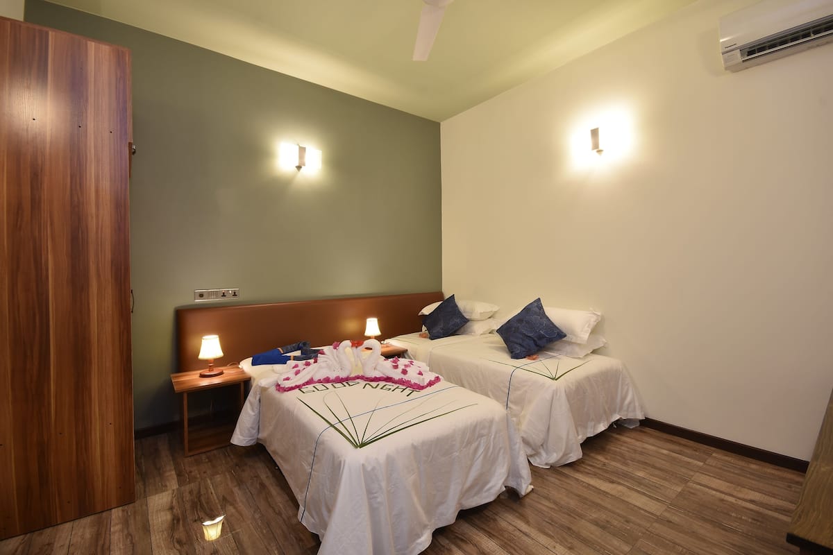 Ein Hotelzimmer mit zwei Betten, einem Holzschrank, einem Nachttisch mit Lampe und einer Wandklimaanlage.