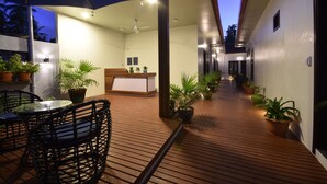 Un espacio al aire libre techado con piso de madera, muebles de mimbre negro y plantas en macetas.