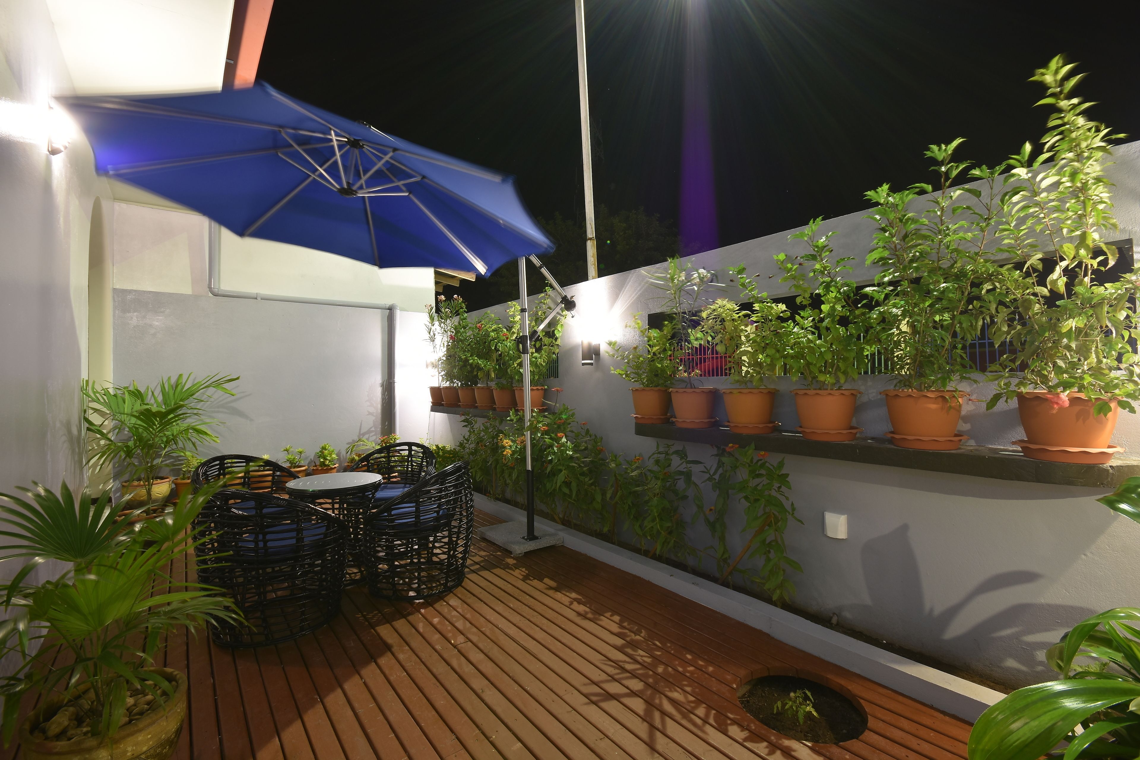 Un espace patio aménagé avec une table et des chaises, des plantes en pot et un parasol bleu.