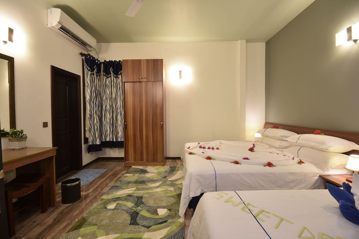 Ein Hotelzimmer mit zwei Betten, einem Holzschrank, einem Schreibtisch mit Stuhl und einer kleinen Mülleimer.