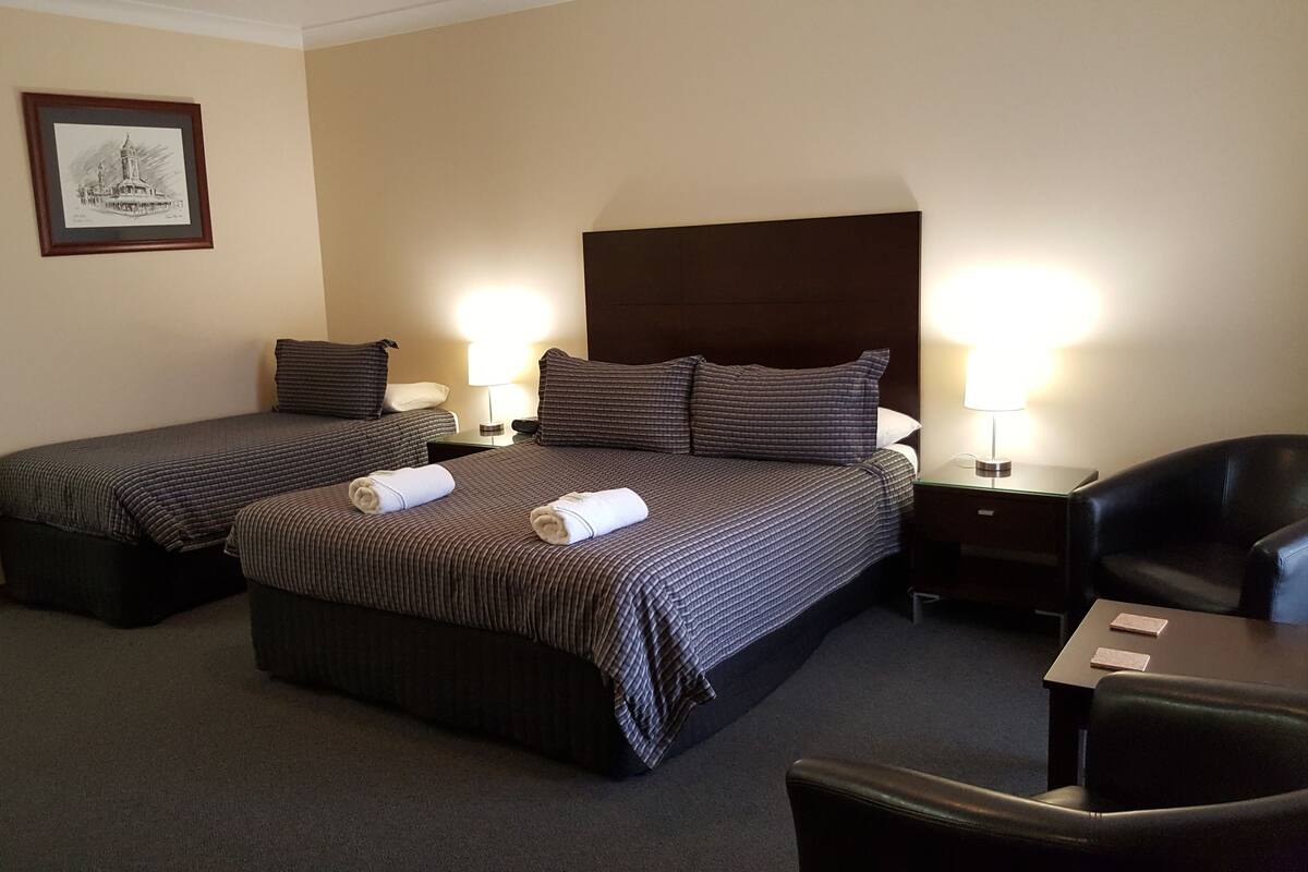 A hotel room with two single beds, a large bed, a desk, a chair, and a framed picture on the wall.