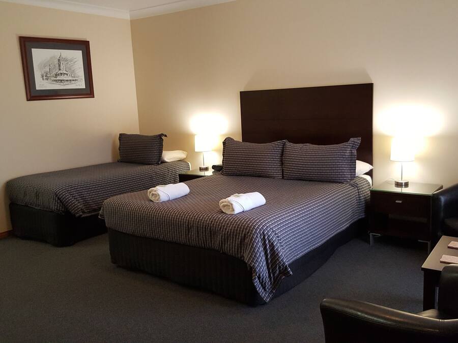 A hotel room with two single beds, a large bed, a desk, a chair, and a framed picture on the wall.
