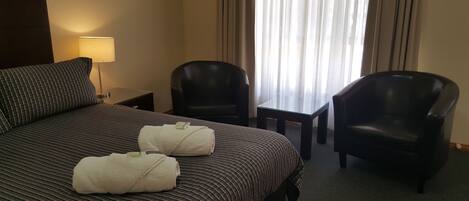 Habitación de hotel con una cama grande, dos sillones de cuero negro, una mesita y una lámpara.