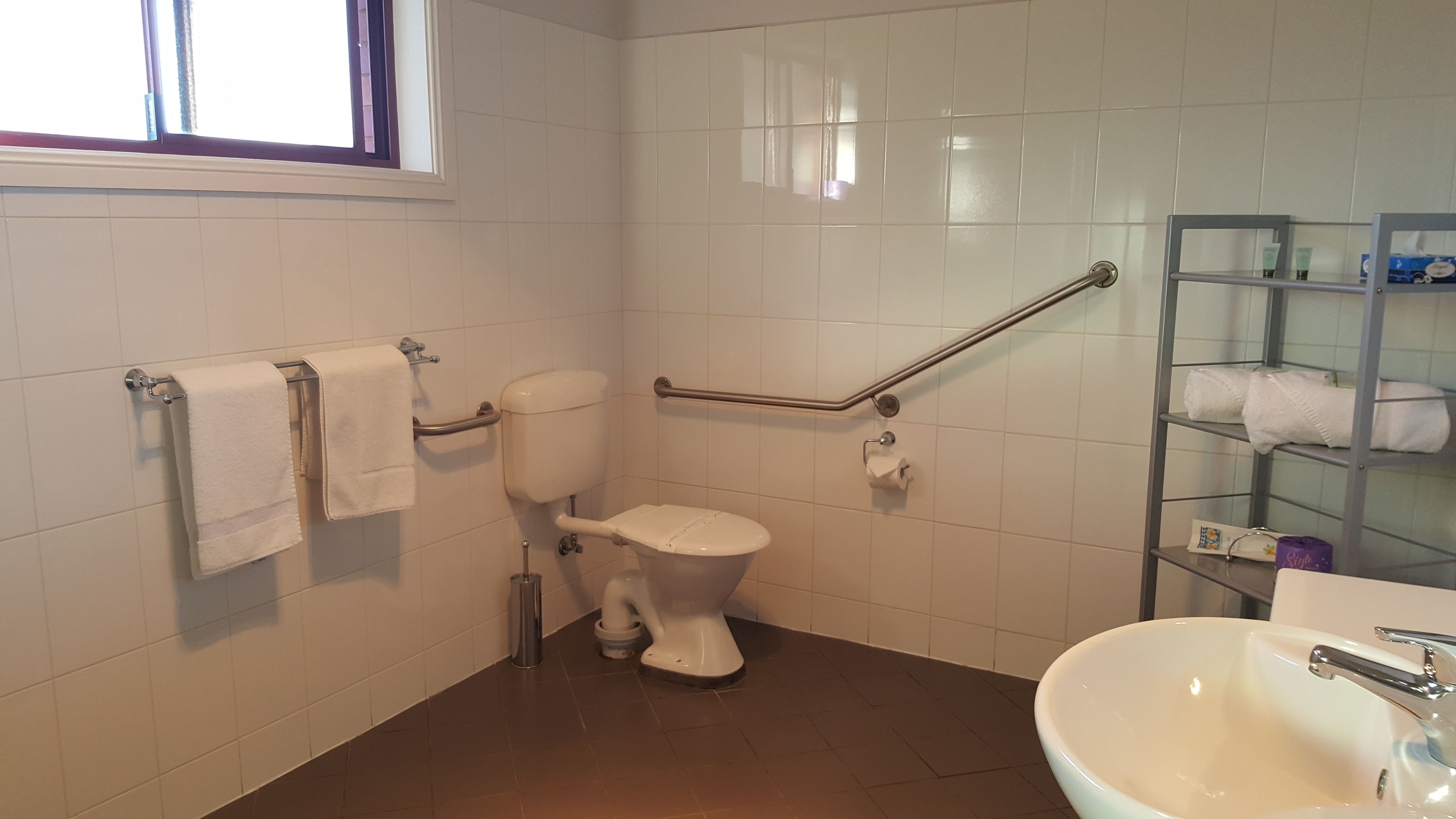 Un bagno con il water, una maniglia di sostegno, un lavandino e uno scaffale con asciugamani.