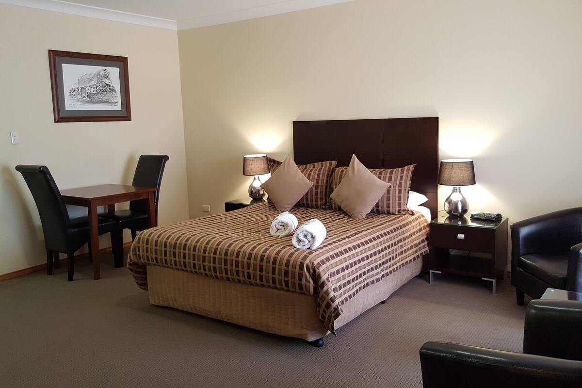 A hotel room with a bed, two bedside tables with lamps, a desk with a chair, and a framed picture on the wall.