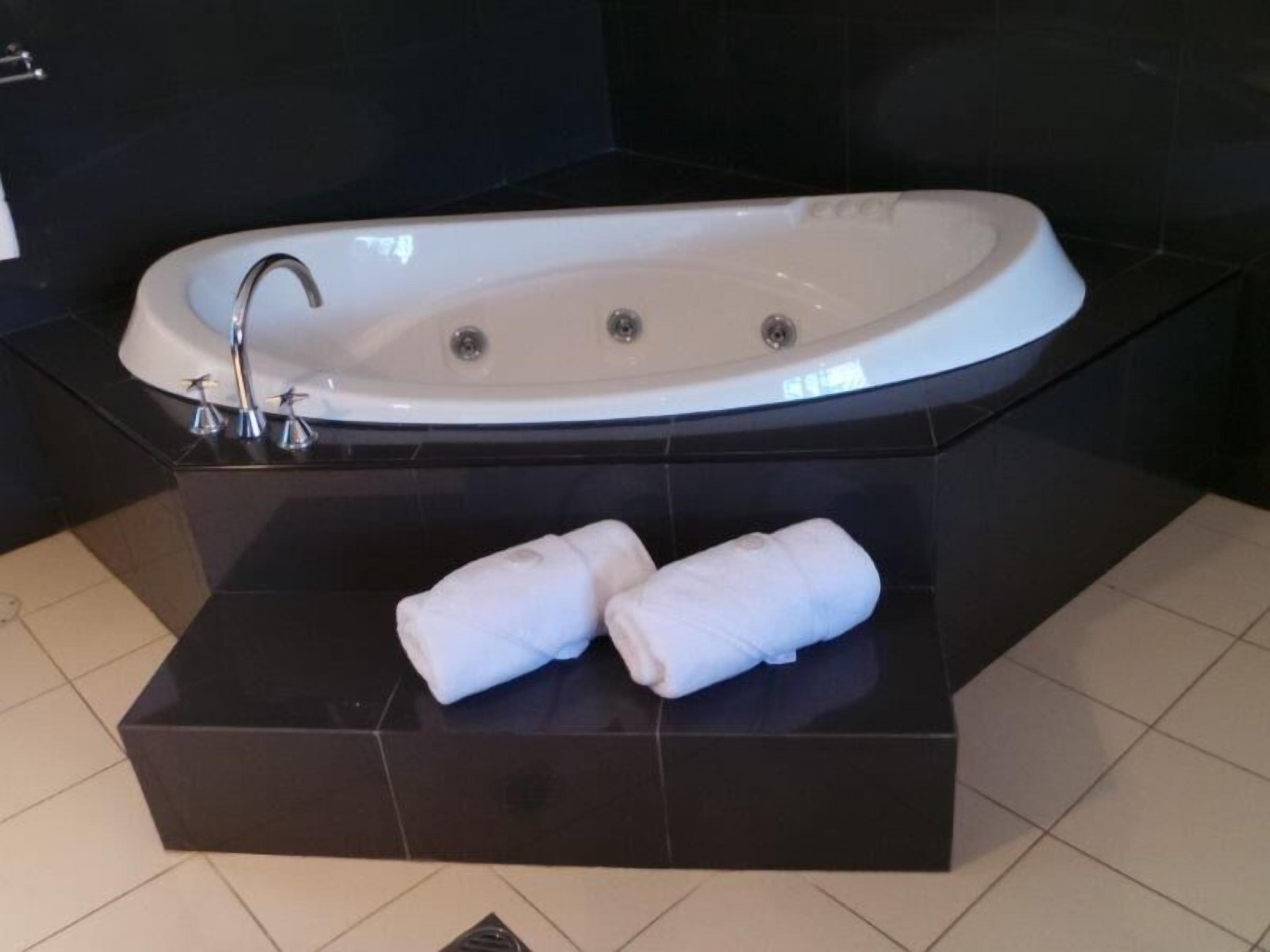 A modern bathroom with a freestanding bathtub, a black sink, and two rolled towels on a black platform.
