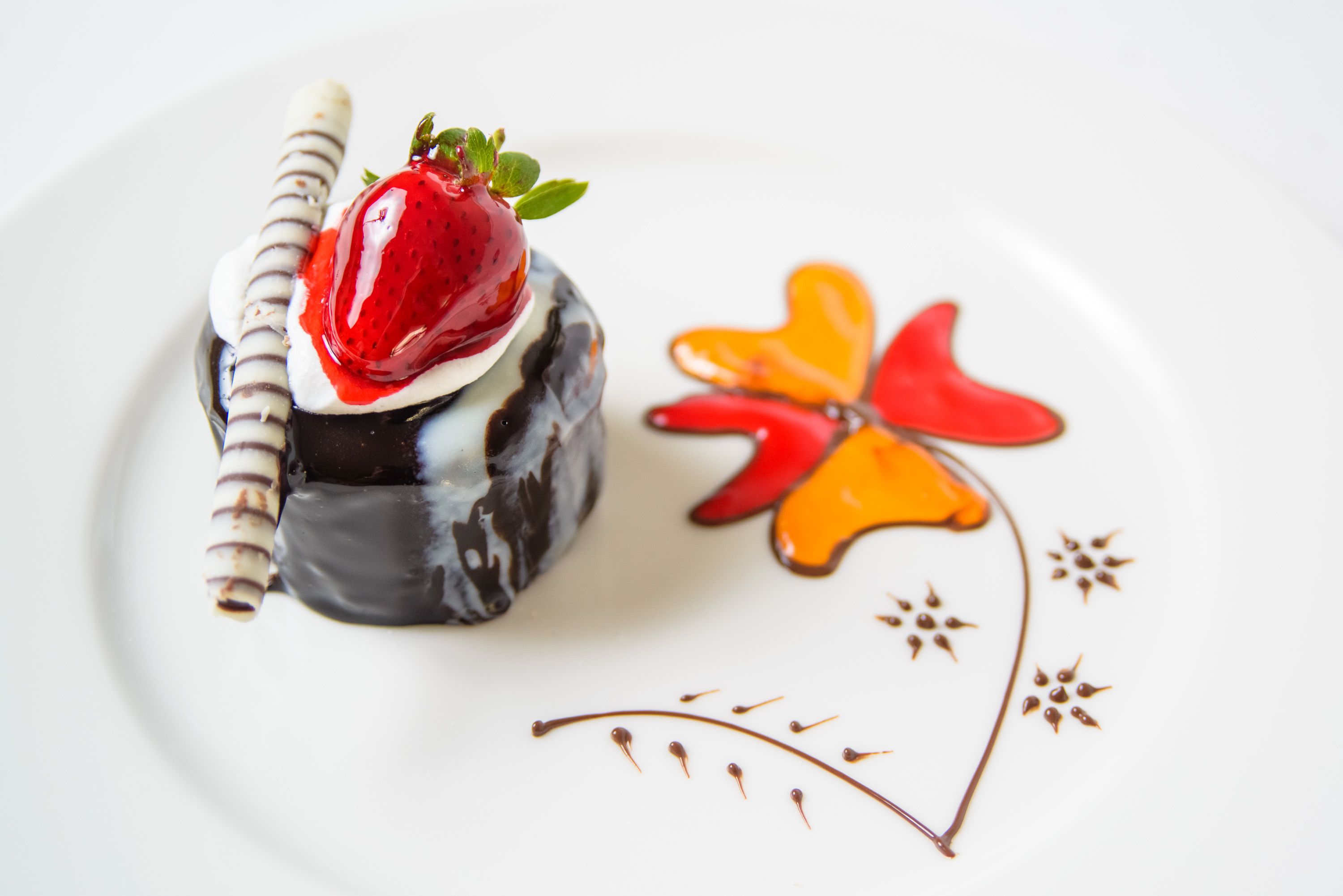 Un dessert composé d’une fraise, de chocolat et d’une fleur décorative, le tout présenté sur une assiette blanche.