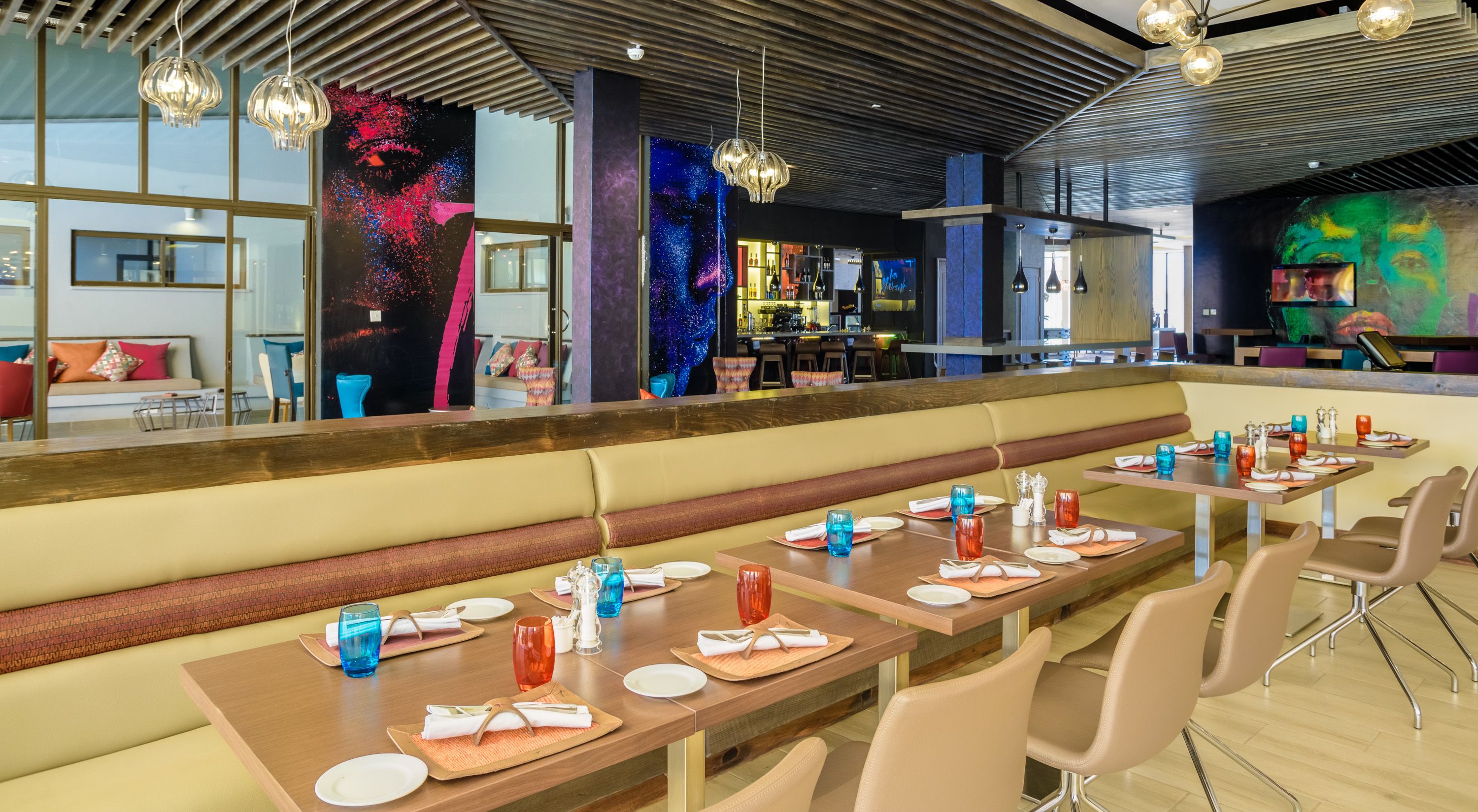 Un restaurante moderno con mesas comunitarias largas, zona de bar y arte mural llamativo.