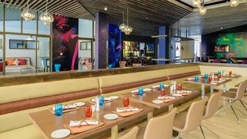 Un restaurante moderno con mesas comunitarias largas, zona de bar y arte mural llamativo.