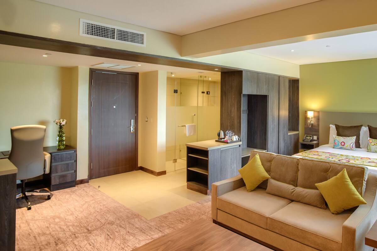 A modern hotel room with a sofa, a bed, a desk, and a bathroom.